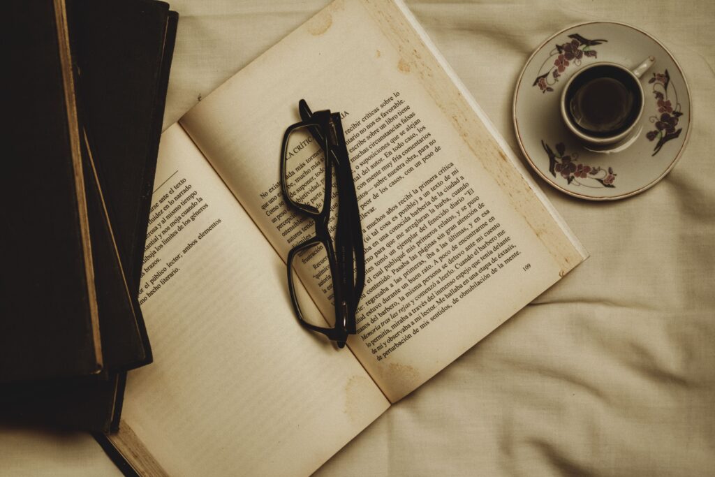 A warm atmosphere of relaxation featuring an open book, eyeglasses, and a cup of coffee on a saucer.