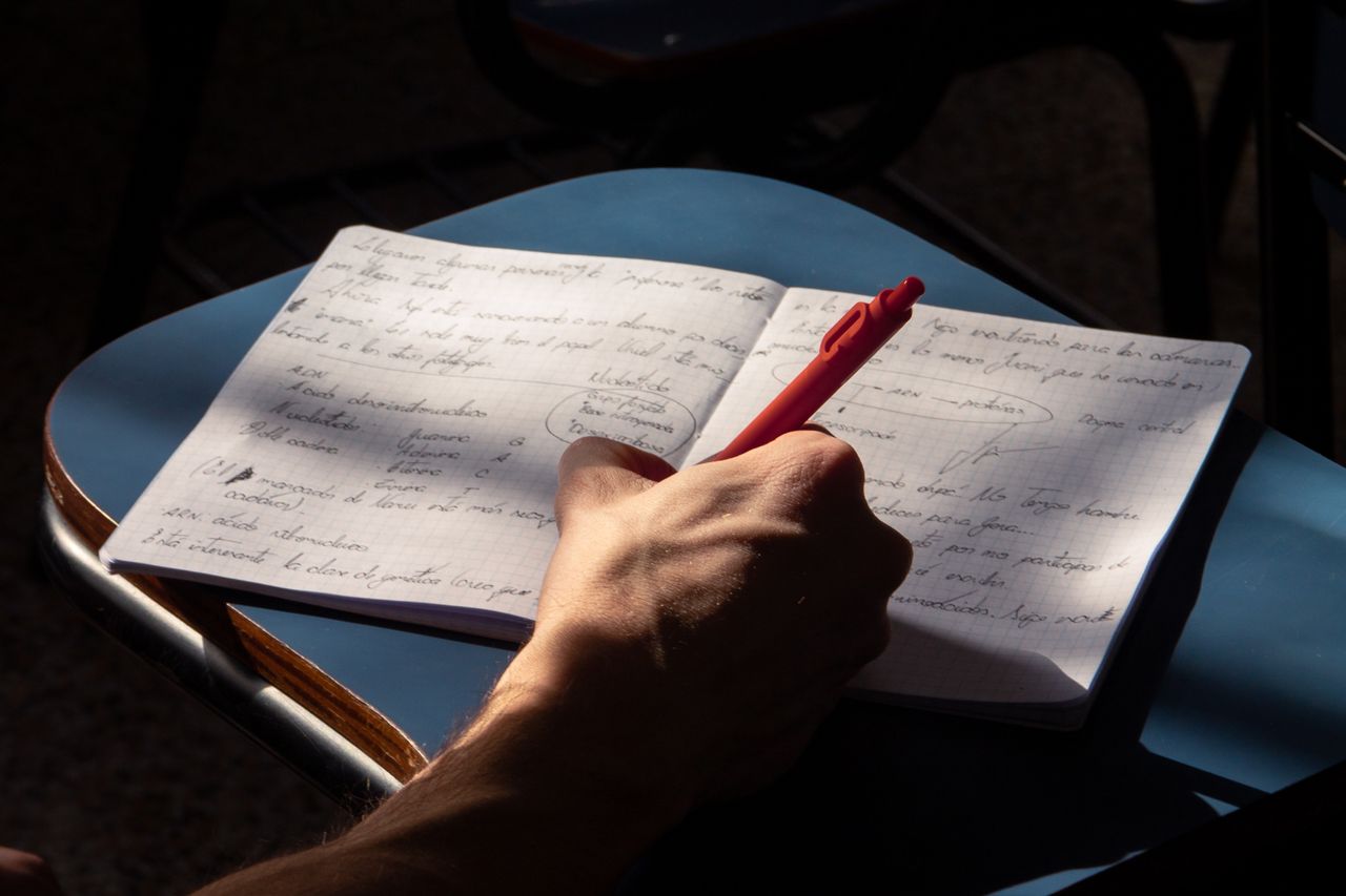 ours-journey Handwriting notes with a pen on an open laptop desk in warm daylight.