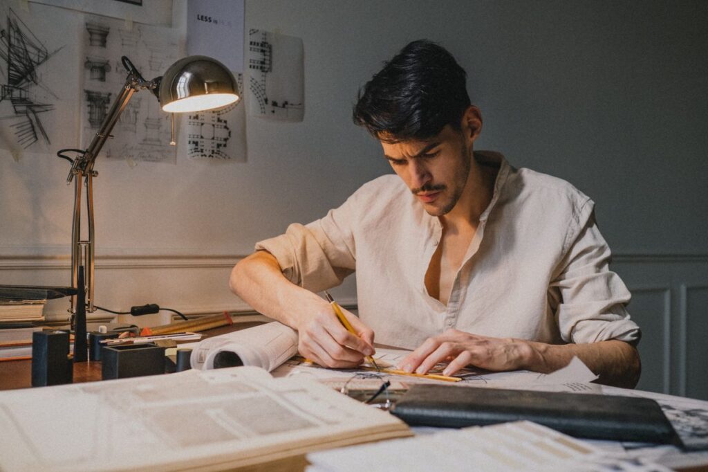 pexels photo 9617384 9617384 A focused architect sketching designs at a desk, illuminated by a lamp indoors.